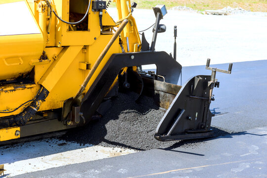 Road construction equipment lays asphalt on new road surface at worksite