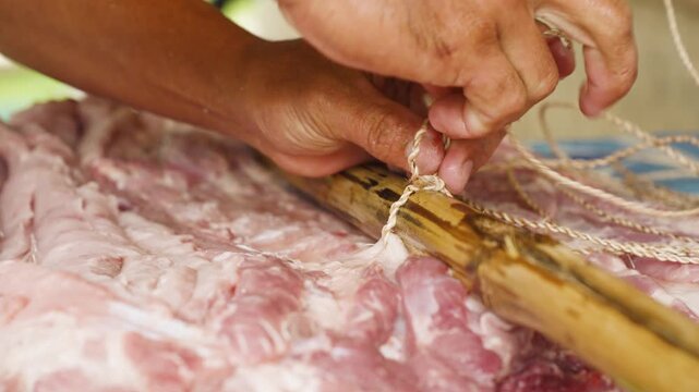 Close-Up of Hands Tying the Pork Belly and Securing It with Bamboo Poles for Grilling
