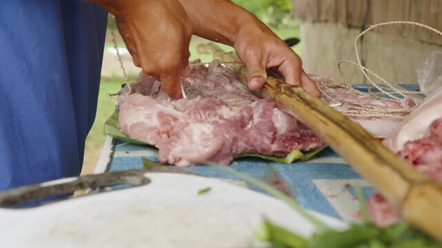 Person Stitching Pork Belly and Securing It with Bamboo Poles for Grilling