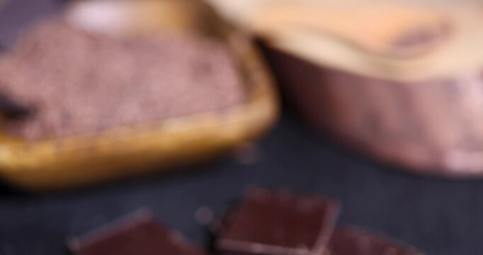 Dark chocolate chunks on kitchen table, ground grated chocolate crumbs inside wood container near brown cocoa food pieces