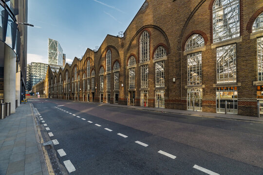 View of the historic brick facade of the former Billingsgate Market building with its distinctive arched windows and modern skyscrapers in London, England, United Kingdom.
