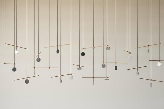 Large scale kinetic installation featuring numerous thin metal rods and small circular discs hanging from wires against a neutral background
