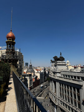 MADRID, SPAIN - JULY 15, 2025: Elevated view of Calle de Alcala featuring historic architecture, the iconic roof quadriga statue, street traffic, and the Generali Seguros building under a blue sky.

