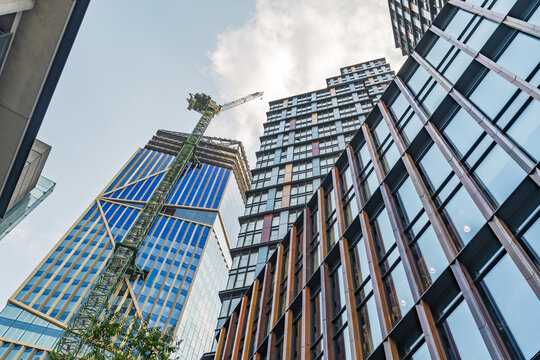 View of modern skyscrapers and a construction crane in the City of London, featuring glass facades and steel structures against a clear sky in London, England, United Kingdom.