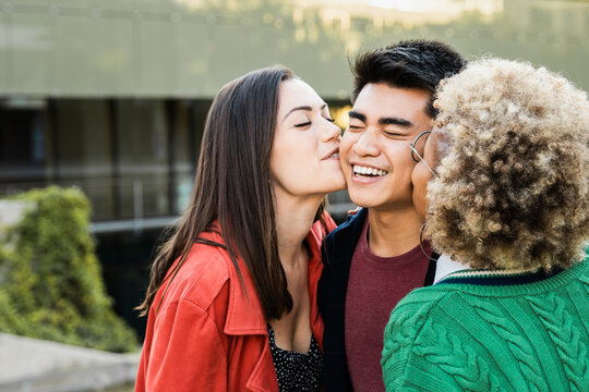Diverse friends kissing asian male guy on the cheek - Young people having fun together outdoors - Youth lifestyle and friendship