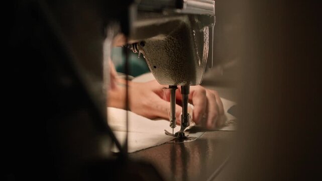 Close-up footage of a person operating an industrial sewing machine, guiding fabric carefully through the needle for garment production, textile craftsmanship, tailoring, and handmade manufacturing.