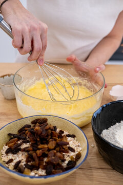 Cooking food. Whisking process. Female chef hand mixing yellow ingredients batter for homemade dough in glass bowl on wooden table.