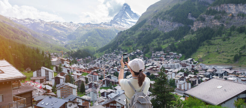 Woman Tourist Exploring Zermatt, Switzerland. Happy Traveler Taking Photo with Smartphone at Zermatt Village Viewpoint and Matterhorn. Popular Tourist Attraction and Travel Destination in Europe