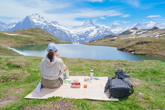Woman tourist enjoying a picnic at Bachalpsee Lake with snow capped Swiss Alps in Grindelwald First, Switzerland. Famous Europe summer hiking destination