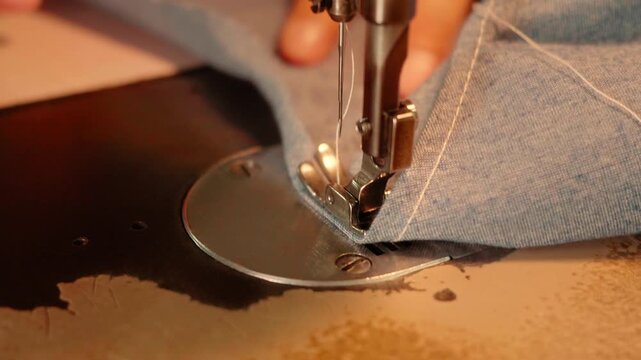 Footage of a close-up sewing machine needle and presser foot guiding blue denim fabric as hands carefully stitch a seam, showcasing vintage craftsmanship.