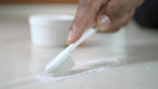 Person Cleaning Tile Grout with Toothbrush and Powder