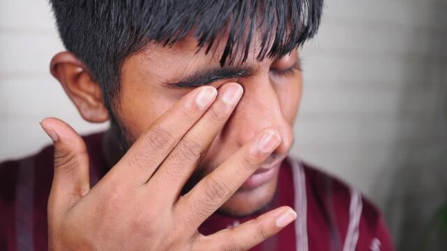 Young man touching his eye in a simple setting