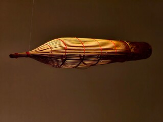 Woven Zeppelin Art Installation: An intricate art piece resembling a zeppelin, crafted from woven natural materials and accented with red thread, hangs suspended against a muted background. © Vixay