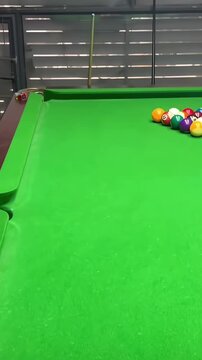 Billiard cue ball striking a colorful cluster of numbered pool balls across a vibrant green felt surface during an intense game of snooker in this high definition motion footage clip which captures th