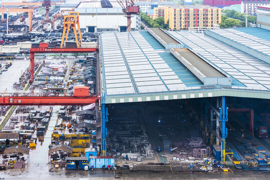 Panoramic view of a large shipyard with extensive industrial infrastructure, a production hall and workers carrying out shipbuilding activities.
