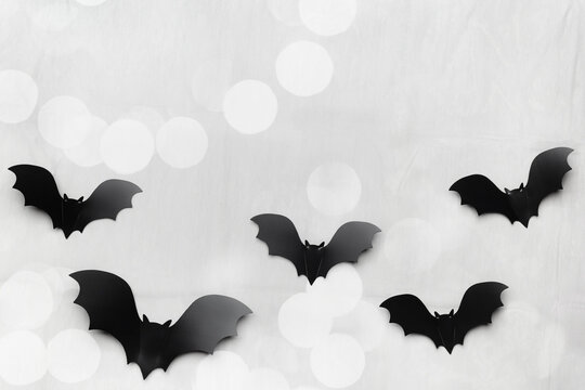 Silhouettes of flying black and dark grey bats on gray background with bokeh. Minimal and spooky holiday pattern for Halloween background, wallpaper, party invitations. Aesthetic top view, flat lay