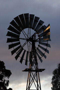 Close telephoto view of a vintage multi-blade farm windmill silhouetted in evening light, classic rural water pump and agricultural infrastructure