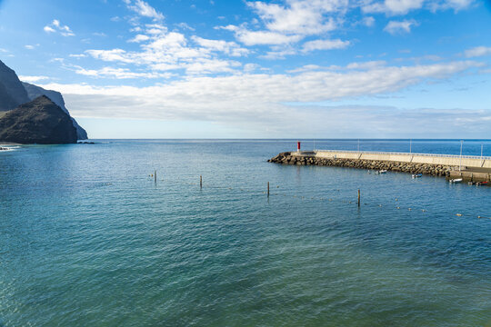 View of the breakwater and lighthouse at La Aldea de San Nicolas with turquoise waters and rocky cliffs under a blue sky in Las Palmas de Gran Canaria, Canary Islands, Spain.