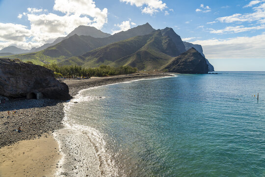 View of La Aldea de San Nicolas featuring a pebble beach, turquoise sea, and rugged mountains under a bright sky in Las Palmas de Gran Canaria, Canary Islands, Spain.
