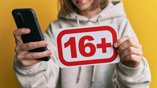 Restricted Content: A young person holding a smartphone displays a 16+ sign, symbolizing age restrictions and content moderation in the digital age.