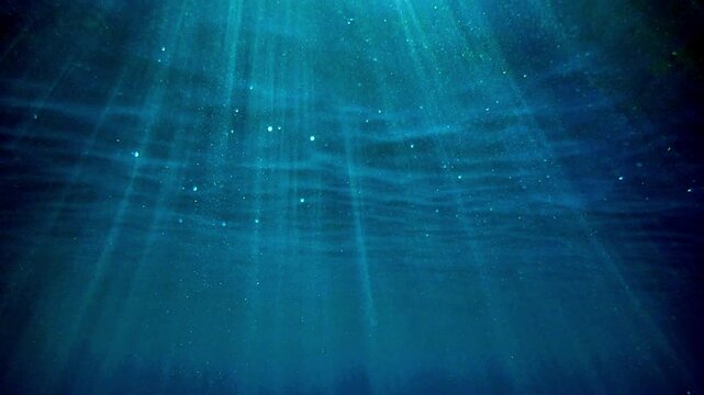 Light filtering down through blue water. Underwater sunlight in deep sea. Sunlight viewed from blue abyss, slow motion. Underwater sunlight shining deep under water with ripples on wave surface. sun.