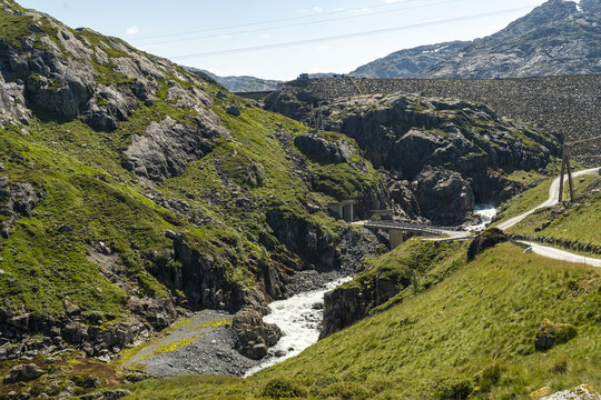View of the Blafalli kraftwerk hydroelectric power plant nestled in a rugged mountainous landscape with a flowing river, concrete dam, and green slopes in Matre, Vestland, Norway.