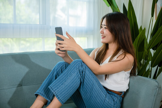 woman checking social media holding smartphone at home while relaxing on sofa living room