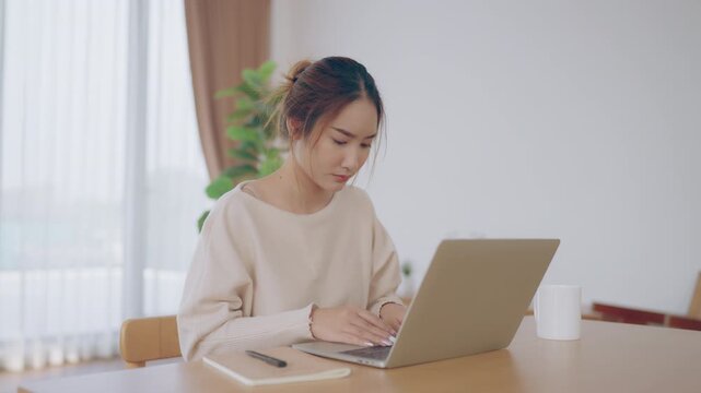 Young Asian woman working in living room, she has a headache due to long and overworking leaving her tired and dizzy. Concept of sickness from work and office syndrome