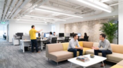 Fototapeta premium Blurred open plan corporate office space with employees sitting on sofa in lounge area having meeting while team members work at desks in background under bright linear lighting