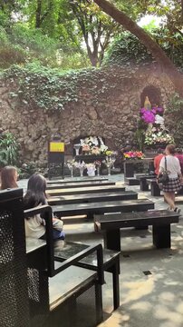 People praying and offering flowers at a Grotto of Our Lady of Lourdes outdoor Marian shrine