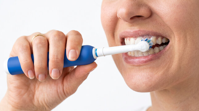 Close up of a woman brushing her healthy white teeth with a blue electric toothbrush isolated on white dental care