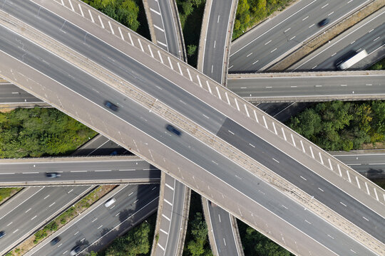 Aerial view of a complex highway interchange with multiple levels of roads and moving vehicles surrounded by lush green trees in the United Kingdom.
