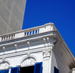 Classic White Building Facade with Ornate Cornice and Blue Shutters Low Angle View © GIL MESHULAM