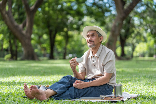 elderly pensioner man spend leisure time relaxing in urban park,sitting,holding tea cup,smiling and looking in nature