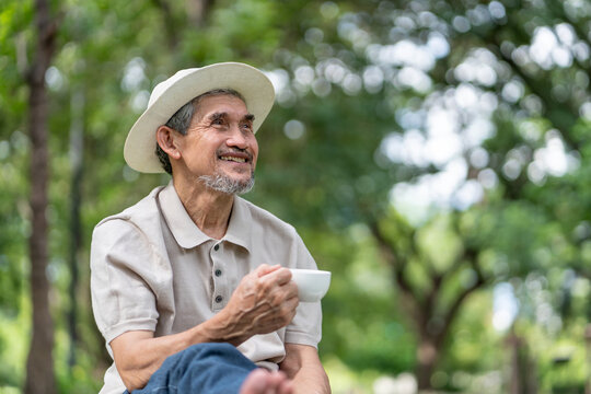 elderly pensioner man spend leisure time relaxing in urban park,sitting,holding tea cup,smiling and looking in nature