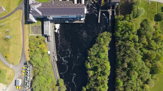 Aerial view rising over Ardnacrusha hydroelectric plant and river, surrounded by greenery