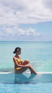 Luxury overwater bungalow hotel room with infinity swimming pool woman looking at ocean view. Travel summer vacation lifestyle. Raw vertical video of real woman model without makeup