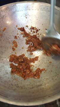 Cooking Thai stir-fried squid with shrimp paste and holy basil. Sauteing sliced shallots, shrimp paste, and seasonings, adding fresh squid rings, tossing with fresh holy basil leaves over high heat in
