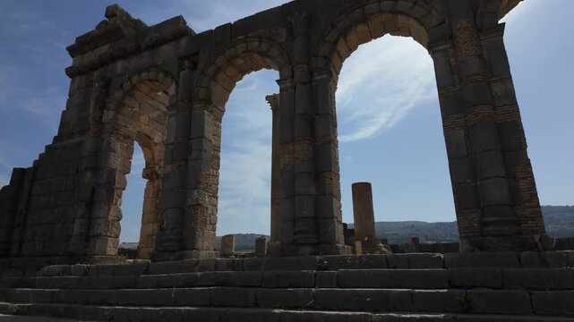 Ground-level cinematic view of the monumental arches of the Basilica of Volubilis, highlighting Roman judicial architecture at Morocco's UNESCO World Heritage archaeological site.