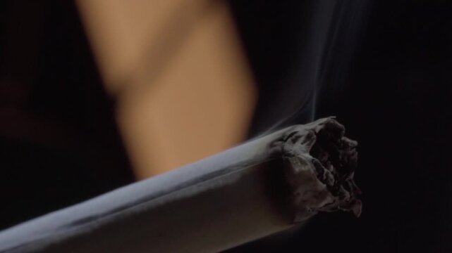 Macro close up of a lit cigar with glowing ash and curling smoke, highlighting slow combustion and rich tobacco texture against a dark background