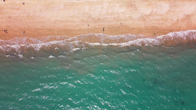 Overhead aerial drone footage of turquoise seawater and foaming waves washing onto the shingle beach at West Bay on Dorset&rsquo;s Jurassic Coast, England. Small beachgoers create a sense of scale within