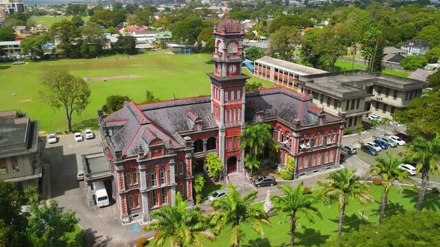 Camera orbits Queen's Royal College, red brick clock tower landmark beside cricket field near Queen's Park Savannah, Port of Spain, Trinidad