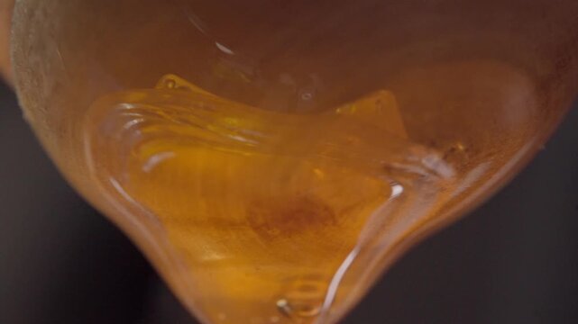 Macro close up of a golden honey droplet suspended before falling, highlighting its natural viscosity and smooth flowing consistency