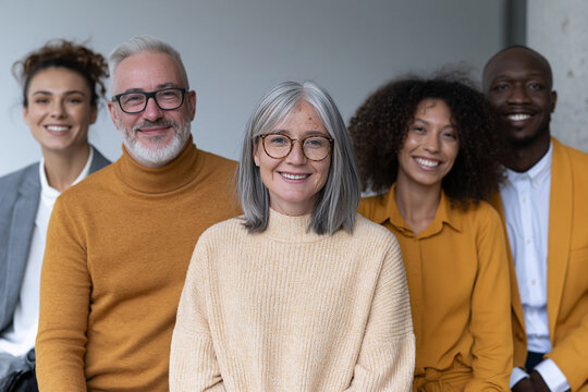 Five people smile warmly, standing close together. They dress in coordinated earthy tones, creating cohesion. Their expressions radiate joy and mutual trust