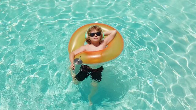 Child floats in swimming pool. Child relaxes in Swimming pool with sunglasses and headphones. Happy child holds a refreshing summer drink in Swimming pool. Young child enjoys sunny water in Swimming
