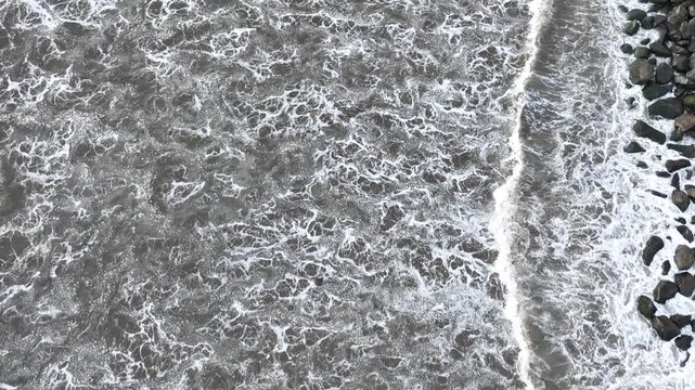 Aerial drone view of turquoise ocean waves breaking into white foam along sandy beach shoreline, cinematic video representing tropical coastal beauty and natural wave pattern motion concept