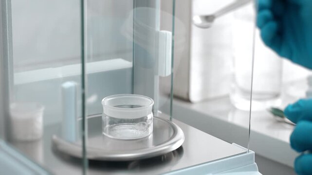 Close-up of laboratory technician adding white granular material to a container on an analytical balance during precise sample preparation and chemical analysis.