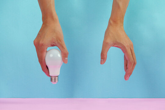 Cropped hands holding LED light bulb on blue and pink background for idea concept