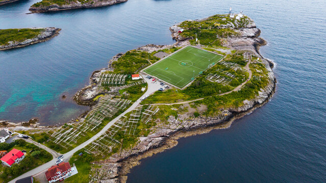 Aerial view of the iconic Henningsvaer football field situated on a rocky island surrounded by the sea with wooden fish drying racks and green landscape in Henningsvaer, Nordland, Norway.