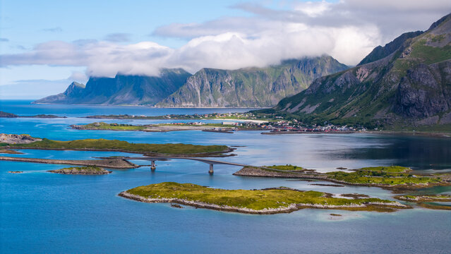 Aerial view of Fredvang Bridges connecting islands with lush green landscapes, rocky mountains, and blue waters in Fredvang, Nordland, Norway.